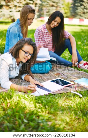 Teenage female making notes in park with her friends on background