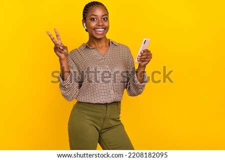 Photo of cheerful positive woman wear plaid shirt headphones holding modern gadget v-sign isolated yellow color background