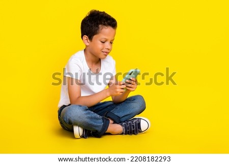 Full size photo of small boy sit look telephone wear t-shirt jeans boots isolated on yellow color background