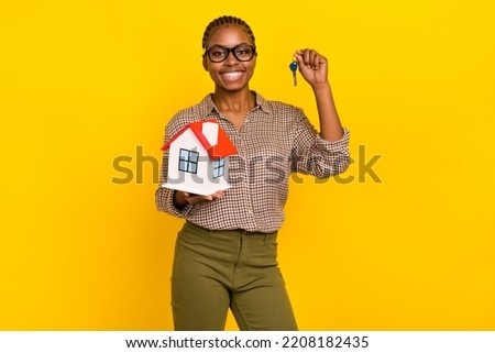 Photo of confident sweet woman wear plaid shirt eyewear holding house rising keys isolated yellow color background