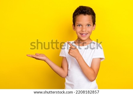 Photo of funny little boy indicate empty space wear white t-shirt isolated on yellow color background