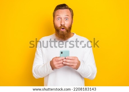Portrait photo of young successful guy bearded red hair hold smartphone youtube funny video reaction wow isolated on yellow color background