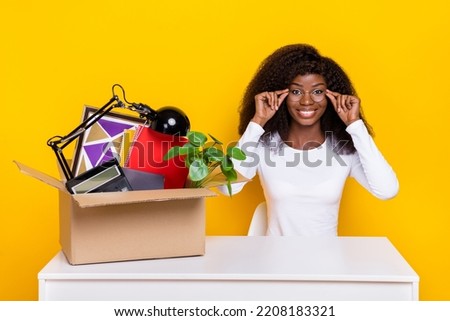 Photo of cheerful pretty lady arms touch eyewear packed stuff box desk isolated on yellow color background