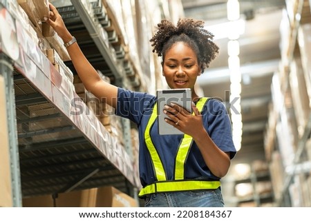 African American woman working with a tablet walks through the warehouse to check inventories and attach a barcode to deliver logistics to customers in a warehouse.