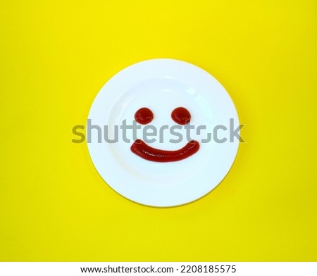 Smile ketchup on white plate on a yellow background. The concept of positive emotions. 