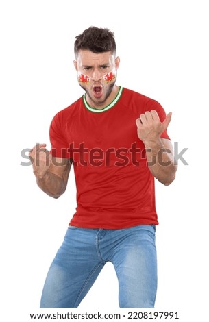 Soccer fan man with red jersey and face painted with the flag of the Wales team screaming with emotion on white background.