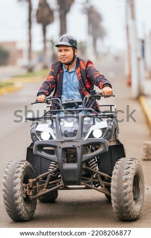 Vertical photo of an adult man driving a quad along a paved road in a city