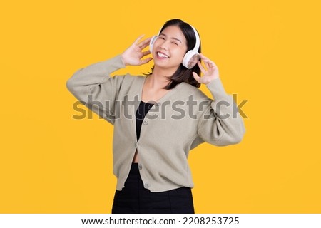 Happy asian beautiful woman listening to music She is wearing wireless headphones and standing isolated on a bright yellow background.