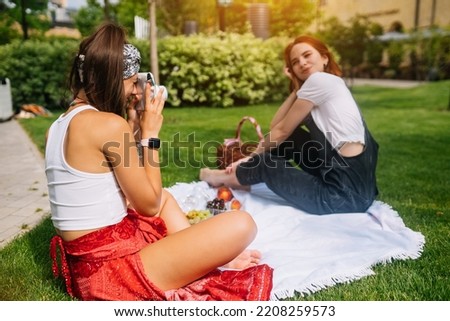 Cool young brunette woman takes photo of girlfriend using camera