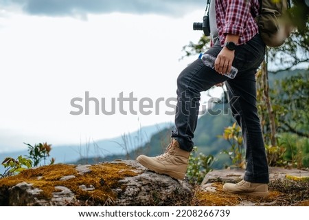 Side view, Close up legs of young asian hiking man standing, camera on kneck and holding water drink bottle with happy on peak of rocky mountain, beautiful landscape in background, copy space Royalty-Free Stock Photo #2208266739