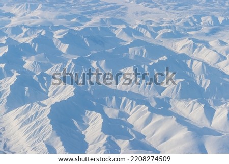 Aerial view of snow-capped mountains. Winter snowy mountain landscape. Air travel to the far North of Russia. Khal-Urekchen ridge, Kolyma Mountains, Magadan Region, Siberia, Russian Far East.