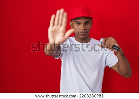 Young hispanic man singing song using microphone with open hand doing stop sign with serious and confident expression, defense gesture 