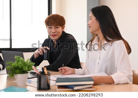 Smiling asian male employee giving some new ideas about project to his colleagues at company meeting