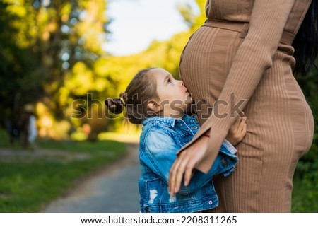 A shot of a Caucasian little girl kissing the belly of his pregnant mother