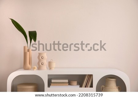 Interior design of aesthetic and elegant room with copy space, modern white commode, books, decoration, vase with leaf and personal accessories. Stylish home decor. Template.  Royalty-Free Stock Photo #2208315739