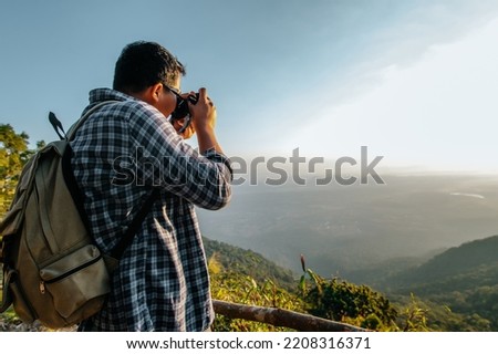 Young Asian hiker man and backpack use camera to take pictures on view point in forest. copy space