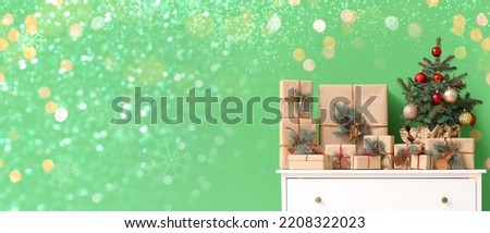 Chest of drawers with Christmas tree and presents near green wall in room