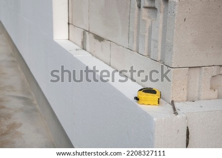 Black yellow tape measure on white rigid polyurethane foam sheet on wall. Thermal insulation. Royalty-Free Stock Photo #2208327111