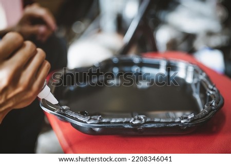 Auto mechanic applying black high-temp RTV silicone gasket maker to oil pan flange. Royalty-Free Stock Photo #2208346041