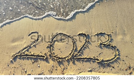 Happy New Year 2023 text on the sea beach. Handwritten inscription 2022 and 2023 on beautiful golden sand beach. Abstract background photo of coming New Year 2023 and leaving year of 2022.