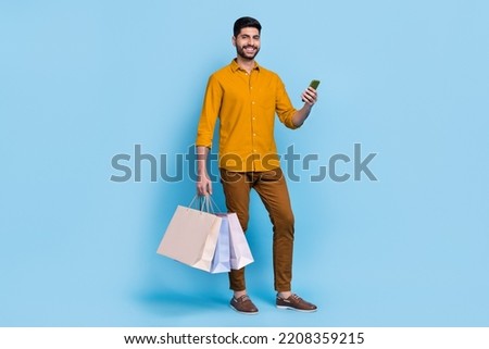 Full body photo of cheerful handsome guy hold telephone packages toothy smile isolated on blue color background