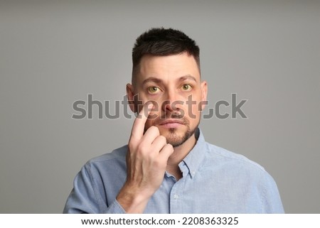 Man checking his health condition on grey background. Yellow eyes as symptom of problems with liver Royalty-Free Stock Photo #2208363325