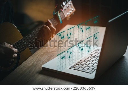 A man playing guitar in living room  while using laptop open chord on website. young guys learning music with a guitar chord table. Royalty-Free Stock Photo #2208365639