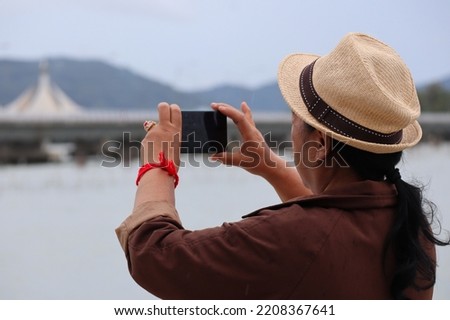 female back view Asian elderly Use your smartphone to take pictures of the sea. Retirement tourism