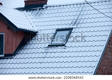 Roof with skylight and black metal shingles covered with white winter snow
