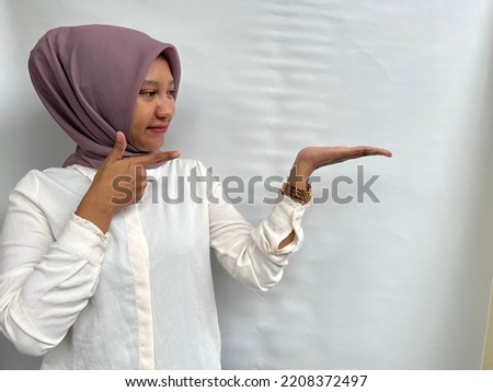 Portrait of smiling beautiful asian woman pointing to copy space. Indonesian woman wearing broken white shirt and lilac hijab isolated by white background