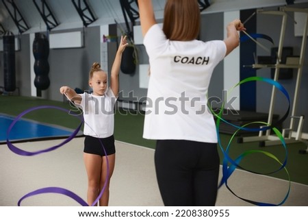 Coaching. Beginner gymnastics athletes doing exercises with gymnastics equipment at sports gym, indoors. Concept of achievements, studying, goals. Female coach training athletes