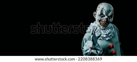 a creepy evil clown, in a gray costume with a white ruff around his neck, against a black background with some blank space on the left, in a panoramic format to use as web banner or header Royalty-Free Stock Photo #2208388369