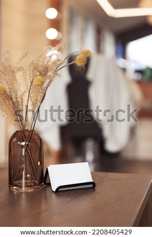 Barber business cards near glass vase with dried flowers on wooden table in hairdressing salon. Space for text
