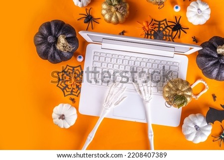 Funny Halloween workplace with laptop flat lay. Office corporation Halloween party invitation, blogger autumn holiday background. White laptop with Halloween party decor, orange background top view