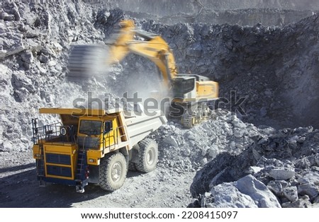 Excavator pours stones into the body of a mining truck, close-up. The image of the excavator in motion is blurred due to the long exposure and is fuzzy.