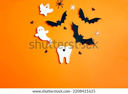 White funny creepy tooth with Halloween decorations on orange background. Dentist Halloween concept. Top view, flat lay.