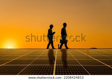 Silhouette engineers walking on roof inspect and check solar cell panel by hold equipment box ,radio communication, solar cell is smart grid ecology energy sunlight alternative power factory concept. Royalty-Free Stock Photo #2208424853