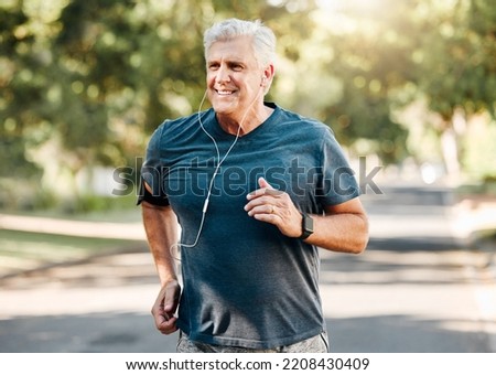 Senior man running while listening to music outdoor street and park for fitness, wellness or healthy lifestyle with summer lens flare bokeh. Elderly person exercise, workout or jogging with earphones Royalty-Free Stock Photo #2208430409