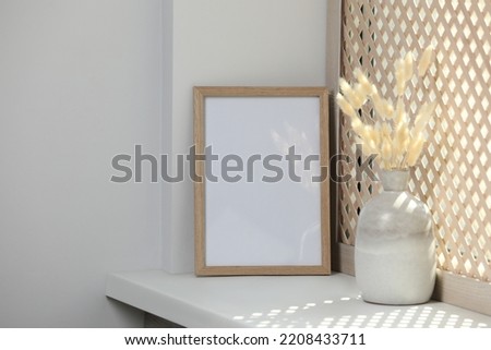 Blank photo frame and vase with dried plant on white window sill. Space for text