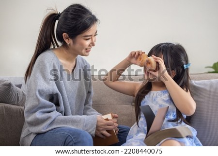 Happy asian mom holding her daughter playing and reading E-book on sofa at home.little girl hugging her mother smile and love having fun at home.Mother day concept