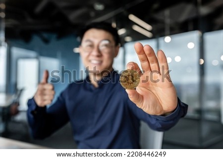 Close up photo of businessman's hand holding cryptocurrency money bitcoin, selective focus man smiling and happy showing thumbs up, working inside modern office building, successful investor