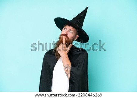 Young wizard in halloween isolated on blue background having doubts while looking up