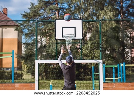 Blond boy in sportswear practices shooting a basketball from behind the three-point line. Outdoor basketball court. Preparing for the season.