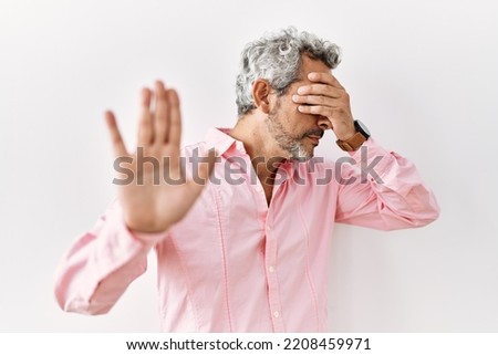 Middle age hispanic man standing over isolated background covering eyes with hands and doing stop gesture with sad and fear expression. embarrassed and negative concept. 