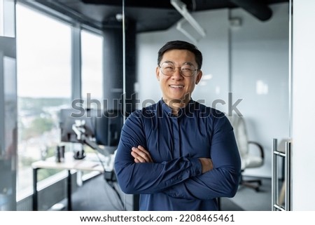 Portrait of successful asian businessman with crossed arms, businessman investor working inside office building loft, looking at camera and smiling, satisfied investor financier