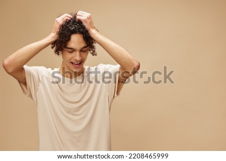 Funny awesome tanned curly man in basic t-shirt touches hair curls posing isolated on over beige pastel background. Fashion New Collection offer. People and Emotions concept. Free place for ad