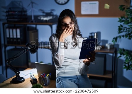 Young brazilian woman using touchpad at night working at the office tired rubbing nose and eyes feeling fatigue and headache. stress and frustration concept. 