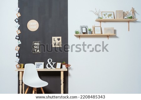 light plastic chair with wooden legs against a black and white wall. classic photo zone for writers in a photo studio. a chair next to a wooden table and pictures on the wall
