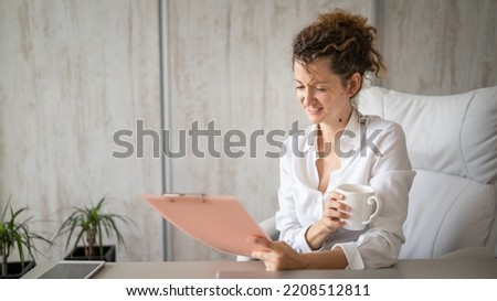 One young woman caucasian female working in the office holding clipboard and drinking coffee modern business woman entrepreneur concept