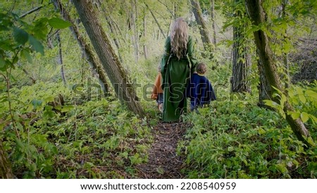 Two little toddler boys cosplay gnomes or hobbits with elf woman walking in green forest. Unrecognizable fairy tale characters. Halloween, kids concept. Amazing light. High quality photo
